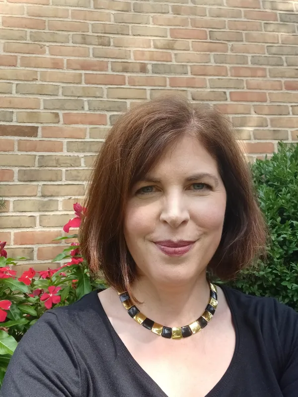 Susan smiling in front of flowers and a brick background